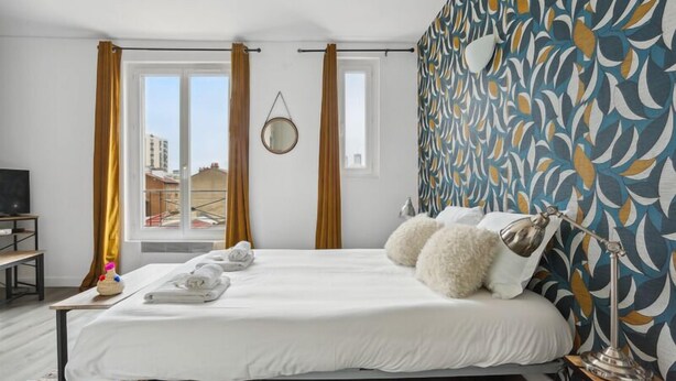 Hotellihuone, jossa on suuri sänky, työpöytä, tuoli, peili ja ikkuna, jossa on verhot.