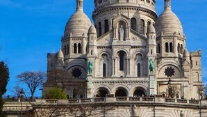 Suuri, historiallinen rakennus, jossa on useita kupoleita ja holvikaaria, todennäköisesti katedraali tai basilika, ja sen edessä on silta.