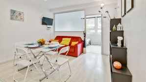 A modern living room with a dining area, a red sofa with yellow cushions, a flat-screen TV, and a large window. - 233 Suite Home Paris Concept (Paris 20 Ménilmontant)