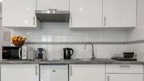 A modern kitchen with white cabinets, a microwave, toaster, kettle, sink, and a small refrigerator. - 233 Suite Home Paris Concept (Paris 20 Ménilmontant)