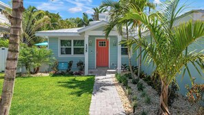 A two-story house with a red door, numbered 125, surrounded by lush greenery and a well-maintained lawn. - Bubbles Up by Beach Boutique Rentals (Holmes Beach)