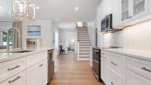 A modern kitchen with white cabinetry, a stainless steel range hood, and a wooden staircase leading to another level. - Bubbles Up by Beach Boutique Rentals (Holmes Beach)