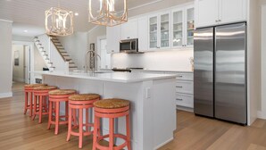 A modern kitchen with white cabinetry, a stainless steel refrigerator, and a central island with bar stools. - Bubbles Up by Beach Boutique Rentals (Holmes Beach)