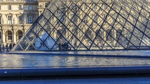 Die Louvre-Pyramide mit freiem Blick auf die umliegende Architektur und einem Springbrunnen im Vordergrund.