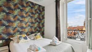 Ein Hotelzimmer mit Bett, Kissen, einem Fenster und Blick auf Gebäude sowie einem Vorhang.