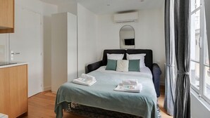 Une chambre à coucher comprenant un lit, une table de chevet, une armoire, un miroir et une fenêtre avec des rideaux.