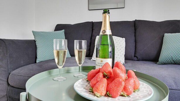 Une table verte avec une bouteille de champagne, deux verres et une assiette de fraises.