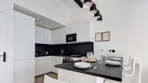 A modern kitchen with white cabinetry, a black countertop, and a dining area with white chairs and a black table.