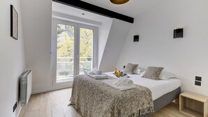 A modern bedroom with a large bed, a view through a window, and a ceiling light.