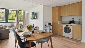 Une cuisine moderne avec des meubles en bois, un lave-linge et un coin repas avec une table dressée pour quatre personnes.