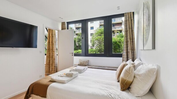 Une chambre moderne avec un grand lit, un téléviseur à écran plat fixé au mur et une fenêtre avec des rideaux.