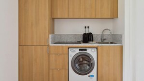 Une cuisine compacte avec des meubles de rangement en bois, un lave-linge, une machine à café et un évier.