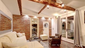 Ein Wohnzimmer mit Backsteinwand, einem weißen Sofa, einem Ledersessel und einer Glastür, die auf einen Balkon führt.