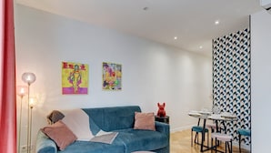 Een moderne woonkamer met een blauwe bank, twee ronde tafels en een eethoek met een behanget patroon.
