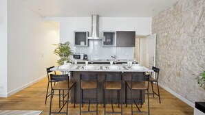 A modern kitchen with a central island, bar stools, and a stone accent wall. - 626 Suite Rambuteau - Superb apartment in Paris (Paris 04 Hôtel-de-Ville)