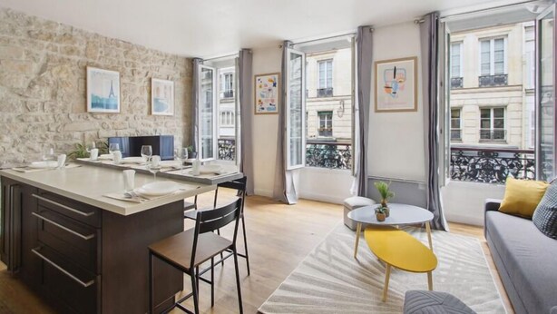 A modern apartment with a kitchen, dining area, and living room. It features large windows, a stone wall, and artwork on the walls. - 626 Suite Rambuteau - Superb apartment in Paris (Paris 04 Hôtel-de-Ville)
