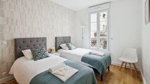 A hotel room with two beds, a balcony, a white chair, and a view of the city. - 626 Suite Rambuteau - Superb apartment in Paris (Paris 04 Hôtel-de-Ville)