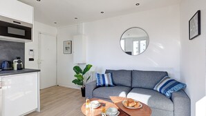 Una sala de estar moderna con un sofá gris, un espejo redondo y una mesa de comedor con alimentos para el desayuno.