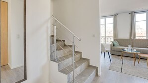 Ein modernes Apartment mit Treppe, einem Wohnbereich mit Sofa und Couchtisch sowie großen Fenstern.