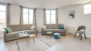 Ein modernes Wohnzimmer mit zwei grauen Sofas, einem runden Couchtisch, einem blauen Hocker und einer Stehlampe.