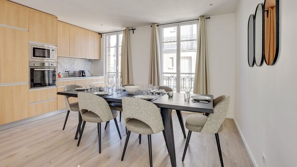 Eine moderne Küche mit integrierten Geräten, ein Essbereich mit Tisch für vier Personen und große Fenster mit Vorhängen.