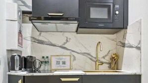 A compact kitchen with dark cabinetry, a microwave, a gas stove, and a sink with a gold faucet. - Suite CD : Superb Parisian apartment (Paris)