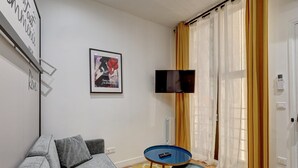 A living room with a sofa, a small table, a TV, and a door with curtains. - Suite CD : Superb Parisian apartment (Paris)