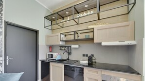 A compact kitchen with a dishwasher, microwave, stove, and a small sink. There is a shelf above the sink with decorative items. - 114 Suite Deby - Superb apartment in Paris (Paris 15 Vaugirard)