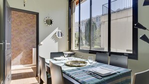 A dining area with a table set for two, a window with a view of buildings, and a door with a floral wallpaper. - 114 Suite Deby - Superb apartment in Paris (Paris 15 Vaugirard)
