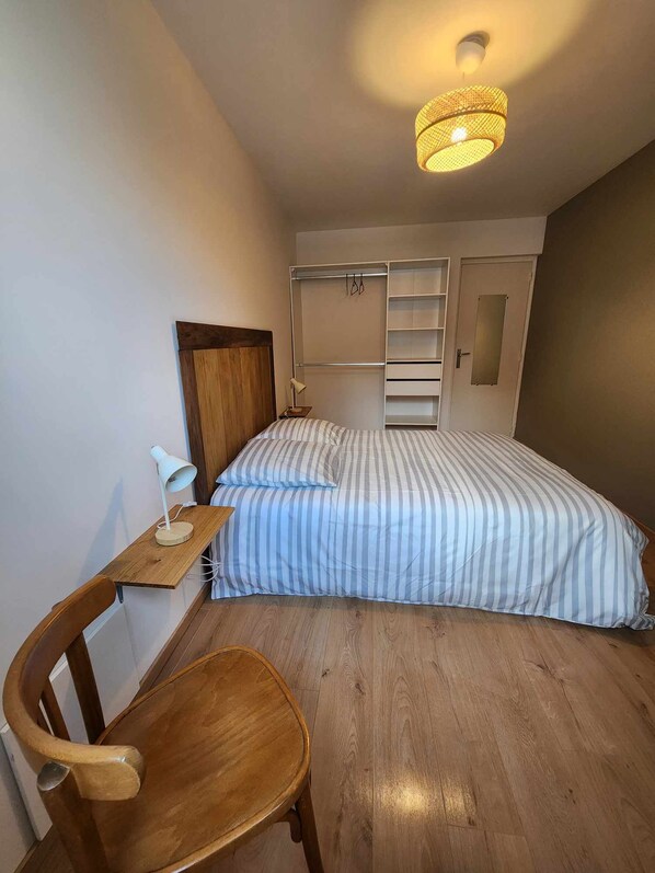 A bedroom with a bed, a wooden chair, a desk with a lamp, and a wardrobe.
