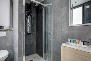 Bathroom features a glass-enclosed shower area with a wall-mounted showerhead and control panel.