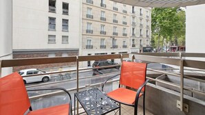 A balcony with two orange chairs and a metal table, overlooking a street with parked cars and a building with multiple windows. - 174 Suite Grenelle - Marvelous apartment in Paris (Paris 15 Vaugirard)