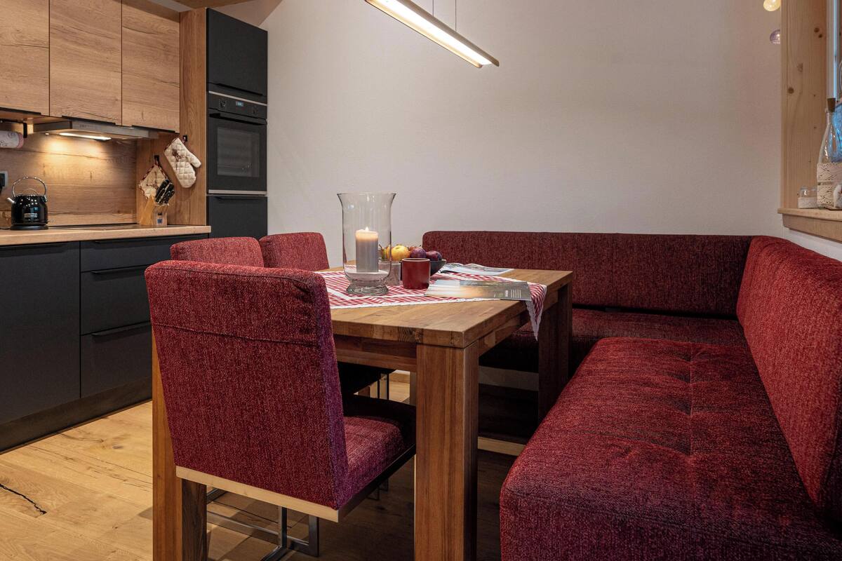 Una cocina moderna con armarios de madera, una mesa de comedor con sillas tapizadas en rojo y una lámpara colgante sobre la mesa.