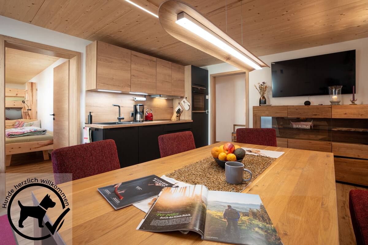Una cocina moderna con armarios de madera, una mesa de comedor con revistas y un televisor montado en la pared.