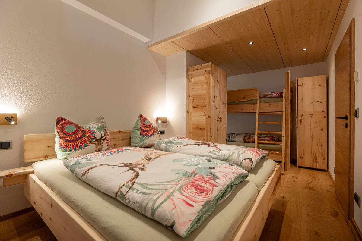 Un dormitorio con una litera de madera, una cama individual con ropa de cama floral y un armario de madera.