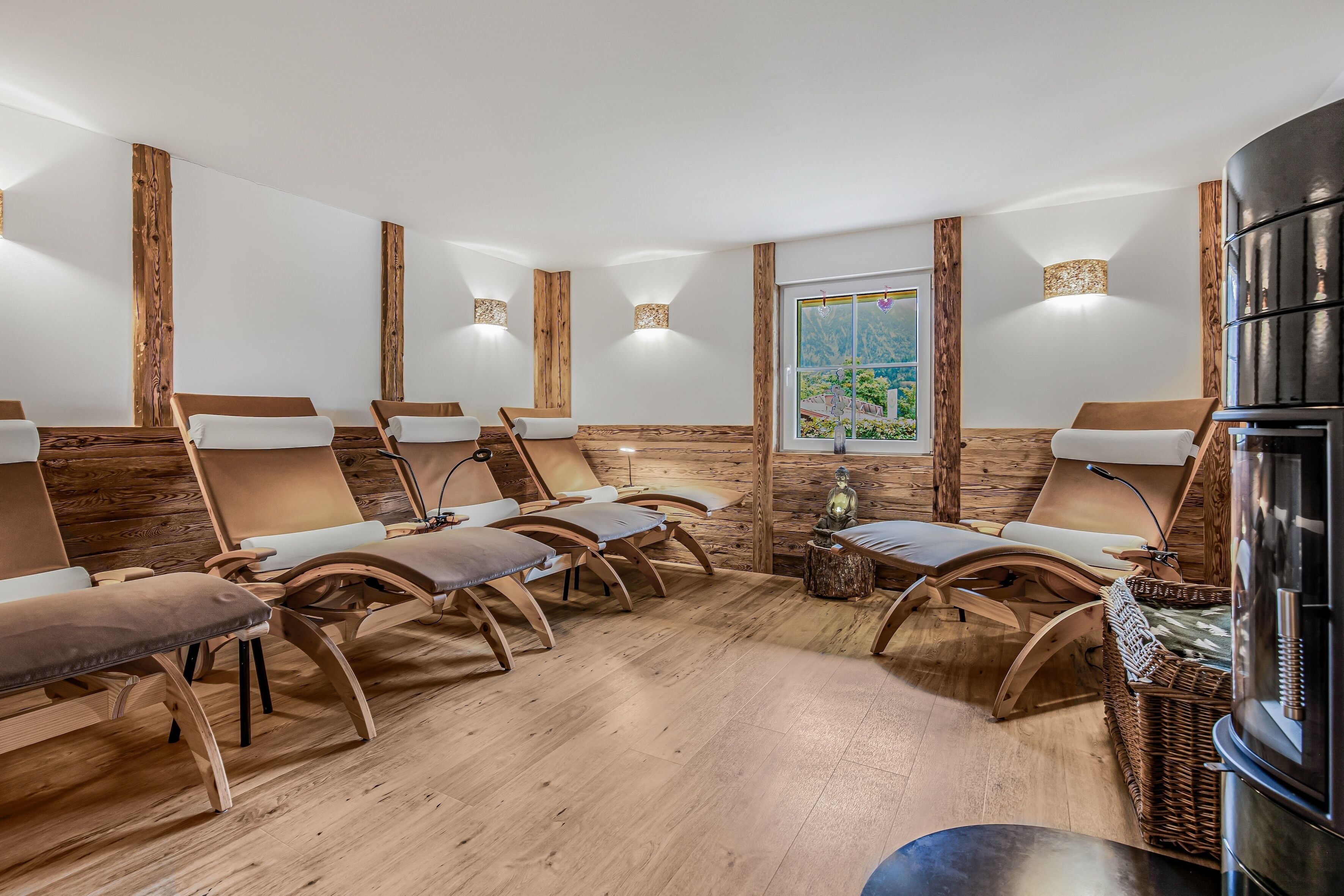 Ein Spa-Raum mit Holzwänden und -decke, mehreren Holzstühlen mit Kissen, einem großen Fenster mit Ausblick und einem schwarzen Schrank.
