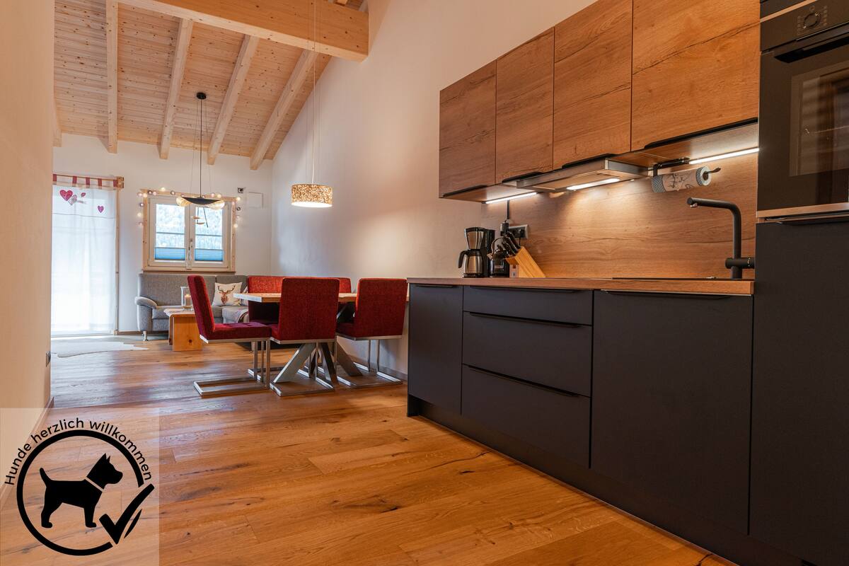 Una cocina moderna con armarios de madera, horno integrado y comedor con sillas rojas.