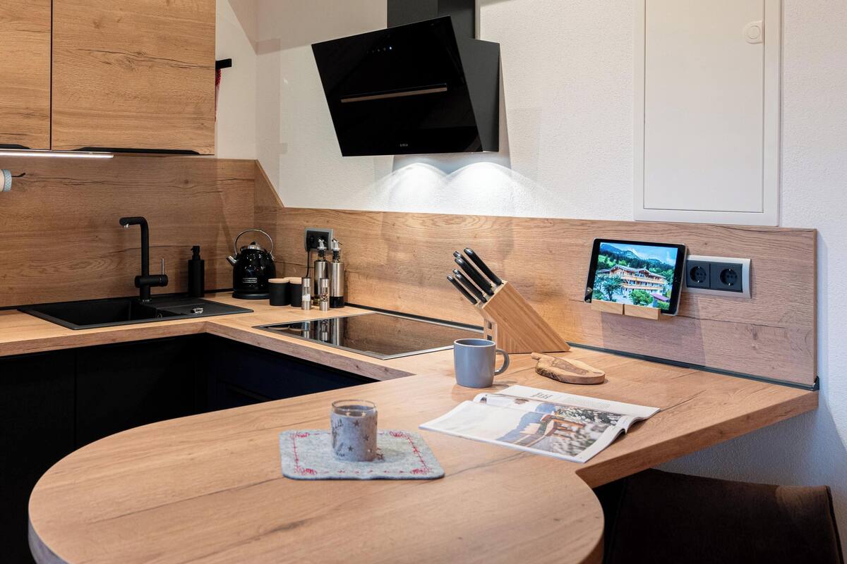 Una cocina moderna con armarios de madera, un lavamanos negro, una estufa integrada y una tableta montada en la pared.