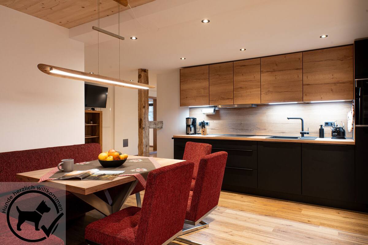 Una cocina moderna con armarios de madera, un lavamanos de acero inoxidable y una zona de comedor con una silla tapizada de rojo.