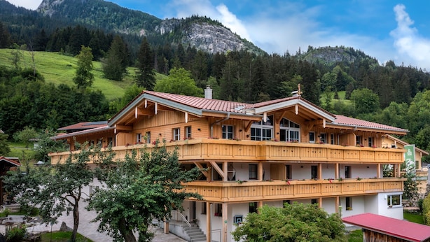 Eine große Holzhütte mit mehreren Balkonen, umgeben von üppiger Vegetation und Bergen.