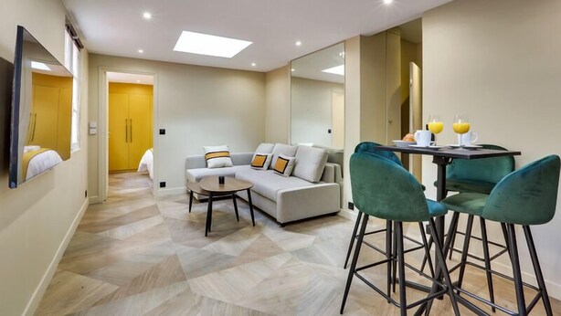 A modern living room with a sofa, a coffee table, and a dining area with two chairs. - 170 Suite Z - Superb apartment in Paris. (Paris 02 Bourse)