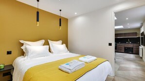 A modern hotel room with a large bed, two pendant lights, and a view into the kitchen area. - 170 Suite Z - Superb apartment in Paris. (Paris 02 Bourse)