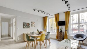 A modern living room with a dining area, a flat-screen TV, and a view of the city. - 215 Suite Esprit Nature - Superb apartment (Paris 02 Bourse)