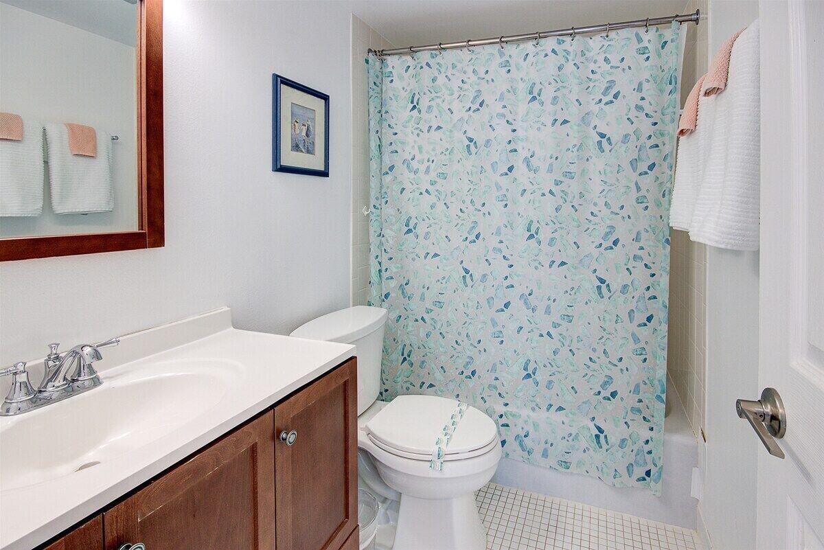 Un baño con un lavabo blanco, un mueble de madera, un inodoro blanco y una cortina de ducha con un estampado azul y blanco.