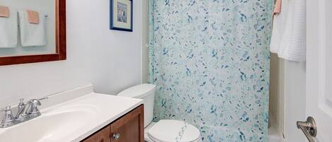 Un baño con un lavabo blanco, un mueble de madera, un inodoro blanco y una cortina de ducha con un estampado azul y blanco.