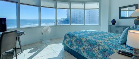 Un dormitorio con una cama grande, un escritorio, una silla, un ventilador de techo y vista al océano.