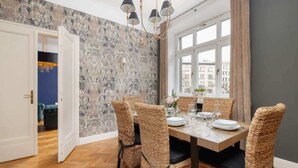Un comedor con un ventanal grande, sillas de mimbre, una mesa de madera dispuesta para cuatro comensales y un papel tapiz estampado.