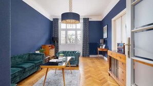 Una sala de estar con una pared azul oscuro, un sofá verde, un aparador de madera y un ventanal grande.
