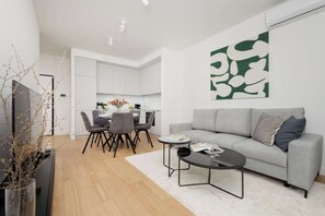 A modern living room with a grey sofa, a coffee table, and a dining area with chairs and a table. - Air-conditioned Apartment | Parking | Center (Warszawa)