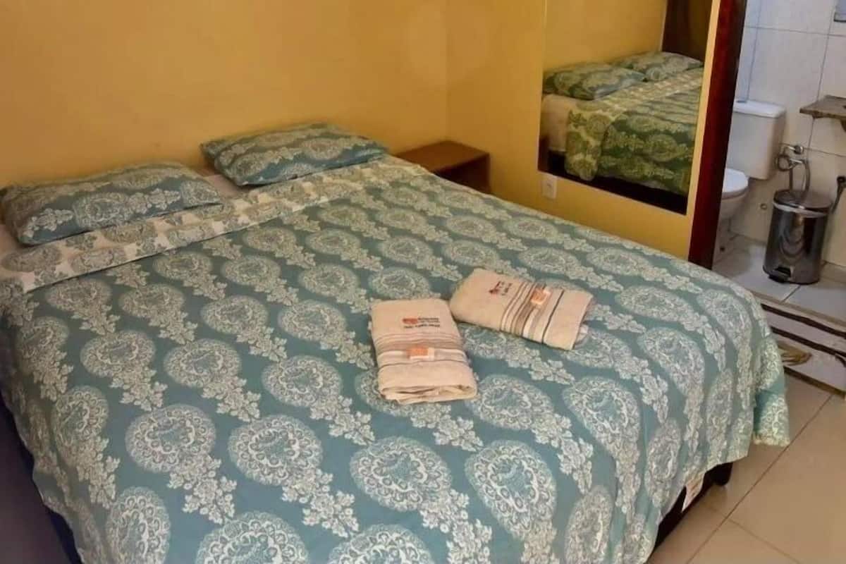 A room with a bed, a nightstand, a mirror, and a toilet.